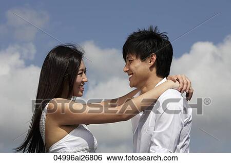 young couple looking at each other and smiling with blue sky as background View Large Photo Image Stock Photograph - young couple looking at each other and smiling with blue sky as background. Fotosearch