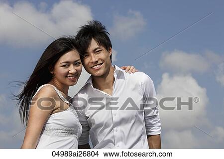 young couple smiling together with blue sky and clouds as background View Large Photo Image Picture - young couple smiling together with blue sky and clouds as background. Fotosearch