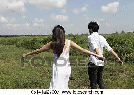 young couple walking in field holding hands, clouds with blue sky as background View Large Photo Image Stock Photo - young couple walking in field holding hands, clouds with blue sky as background. Fotosearch