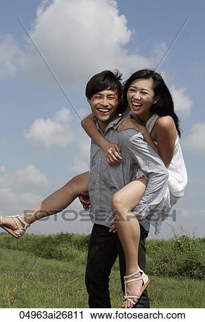 young man carrying a woman on his back laughing with blue sky and clouds in background. View Large Photo Image Stock Image - young man carrying a woman on his back laughing with blue sky and clouds in background.. Fotosearch