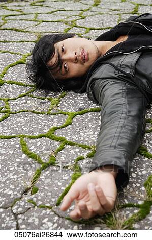 Picture - young man laying on cracked pavement. Fotosearch