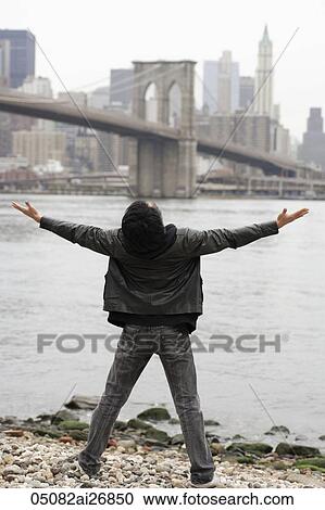 Stock Image - young man looking at city skyline with arms outstretched. Fotosearch