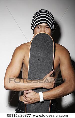 Stock Photo - young man wearing a beanie holding a skateboard over part of his face. Fotosearch