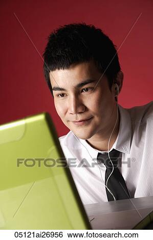 Stock Photograph - young man wearing ear phones looking at lap top. Fotosearch