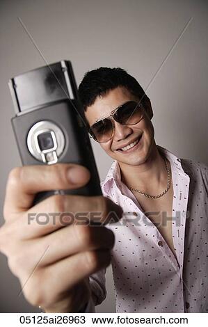Stock Image - young man wearing sunglasses and holding phone out to take a photos. Fotosearch
