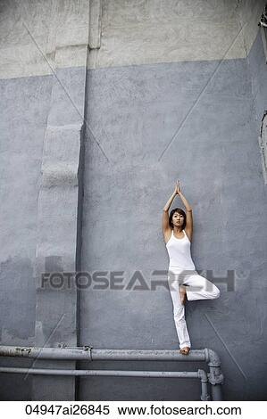Stock Photography - young woman doing yoga standing on a pipe against wall. Fotosearch