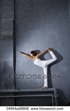 young woman doing yoga while standing on a pipe in front of wall View Large Photo Image Stock Photograph - young woman doing yoga while standing on a pipe in front of wall. Fotosearch