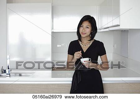 Stock Photo - young woman holding mug in her kitchen. Fotosearch