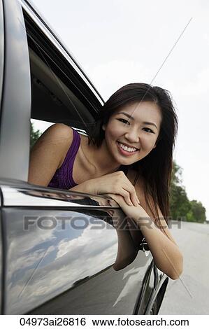 Stock Photograph - young woman leaning out of car window smiling. Fotosearch