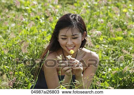 Stock Image - young woman looking at flower in grassy field. Fotosearch