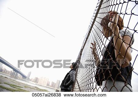 Stock Photo - young woman looking through fence at man on the other side. Fotosearch
