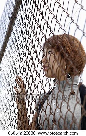 Stock Photograph - young woman looking through fence. Fotosearch
