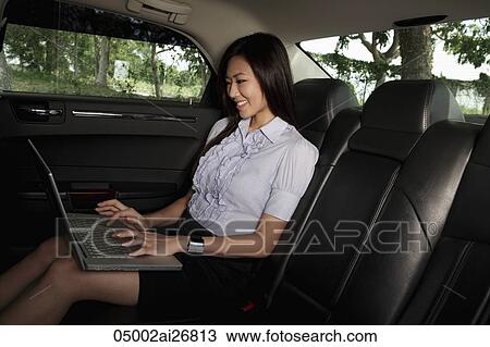 Young woman sitting in back seat of car working on laptop View Large Photo Image Stock Image - Young woman sitting in back seat of car working on laptop. Fotosearch