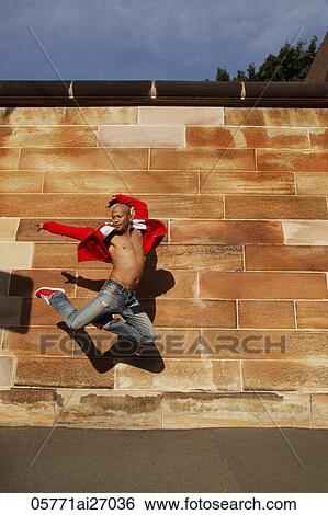 Stock Photograph - Asian man jumping in air in front of brick wall. Fotosearch