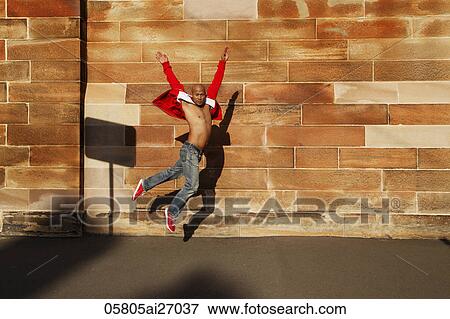 Stock Photo - Asian man jumping in front of brick wall. Fotosearch