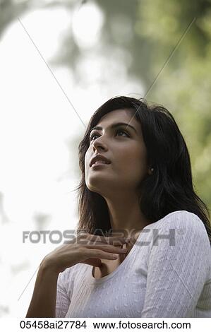 Picture - Back lit head shot of young woman looking up to the sky hand on neck. Fotosearch