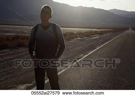 Back lit shot of man standing by the side of a deserted road View Large Photo Image Stock Photo - Back lit shot of man standing by the side of a deserted road. Fotosearch