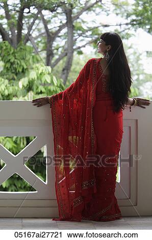 Stock Image - Back shot of Indian woman wearing a red sari looking over balcony.. Fotosearch
