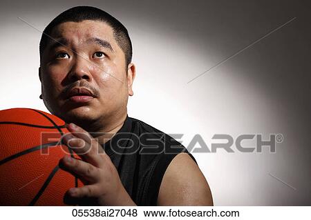 Stock Photo - Chinese man holding basketball and looking up. Fotosearch