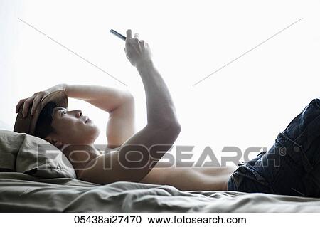 Chinese man laying on bed looking at phone View Large Photo Image Stock Image - Chinese man laying on bed looking at phone. Fotosearch