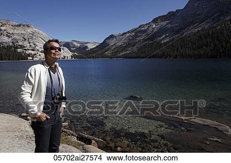 Chinese man standing by lake with camera around his neck View Large Photo Image Picture - Chinese man standing by lake with camera around his neck. Fotosearch