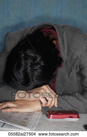 Chinese woman with her head down on table with newspaper and phone View Large Photo Image Picture - Chinese woman with her head down on table with newspaper and phone. Fotosearch