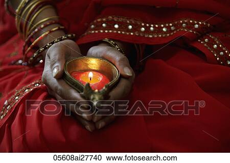 Stock Image - Close up of woman wearing red sari and holding lit candle. Fotosearch