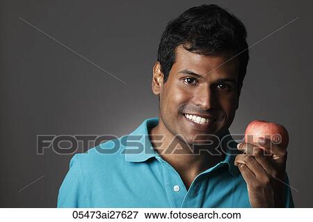 Stock Photo - Head shot of Indian man holding apple and smiling. Fotosearch
