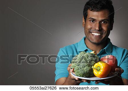 Stock Photograph - Head shot of Indian man holding plate of fruits and vegetables. Fotosearch