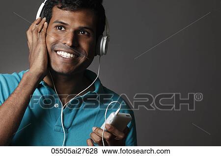Stock Photo - Head shot of Indian man listening to head phones and smiling. Fotosearch