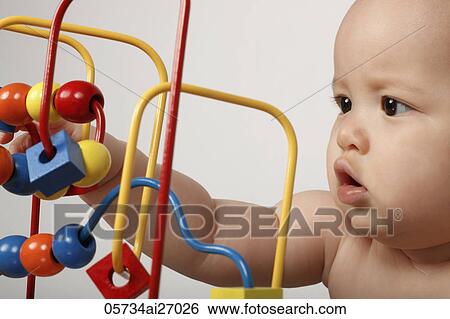 Stock Photograph - head shot of mixed raced baby in profile playing with toy. Fotosearch