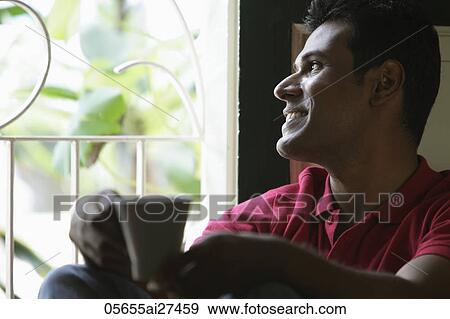 Indian man looking out window smiling holding coffee cup View Large Photo Image Stock Photo - Indian man looking out window smiling holding coffee cup. Fotosearch