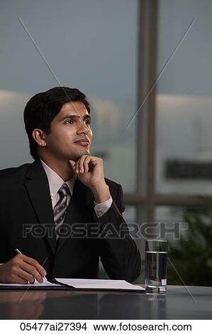 Indian man sitting at desk thinking and writing View Large Photo Image Picture - Indian man sitting at desk thinking and writing. Fotosearch