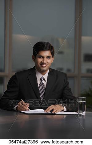 Stock Photograph - Indian man sitting at table writing. Fotosearch