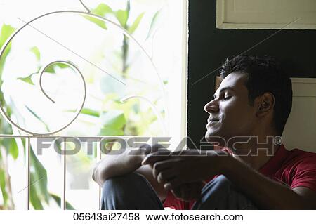 Stock Photo - Indian man sitting near window with closed eyes. Fotosearch