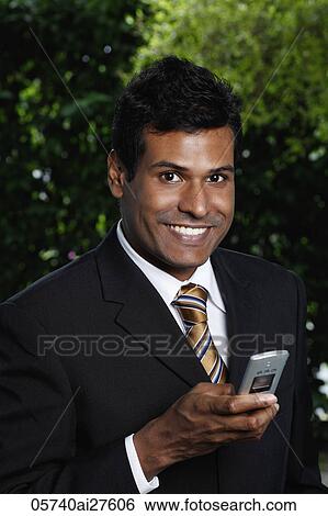 Stock Photograph - Indian man smiling holding phone. Fotosearch
