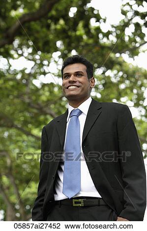 Stock Image - Indian man smiling outdoors with tree in background. Fotosearch