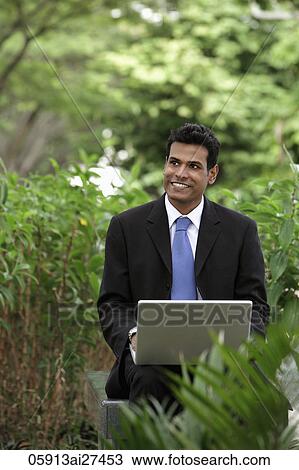 Indian man smiling while working on laptop with green plants in foreground and background View Large Photo Image Stock Image - Indian man smiling while working on laptop with green plants in foreground and background. Fotosearch