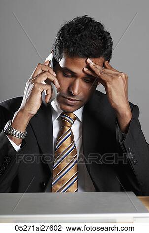 Stock Image - Indian man talking on phone hand on forehead. Fotosearch