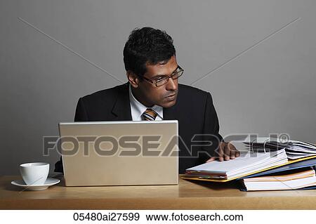 Stock Photo - Indian man working at desk with laptop. Fotosearch