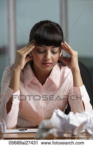 Stock Image - Indian woman holding her head at work. Fotosearch