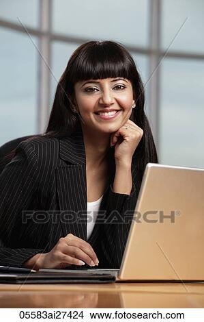 Picture - Indian woman smiling while working on laptop. Fotosearch