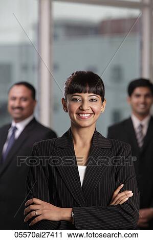Stock Image - Indian woman smiling with arms folded in front of two colleagues. Fotosearch