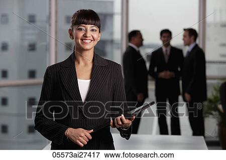 Stock Photo - Indian woman standing in foreground smiling with male colleagues in background. Fotosearch