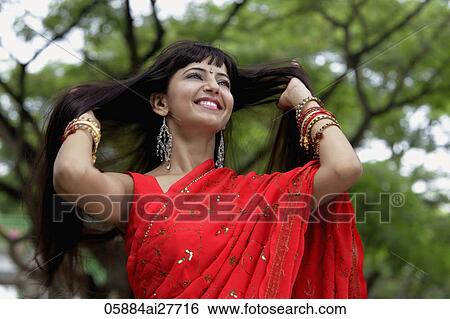 Stock Photograph - Indian woman wearing red sari smiling with hands in hair. Fotosearch