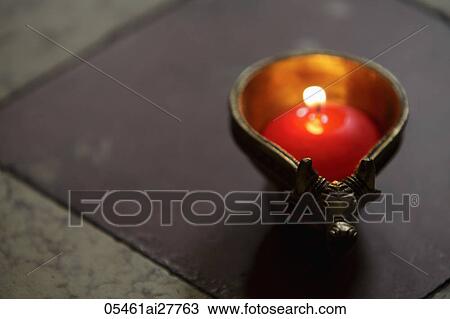 Stock Image - Lit candle in bronze cow dish. Fotosearch