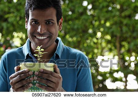 Stock Image - Man holding potted plant and smiling. Fotosearch