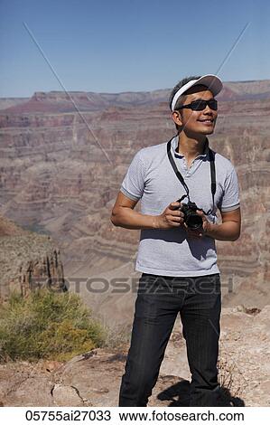 Stock Image - man standing in front of Grand Canyon holding camera. Fotosearch