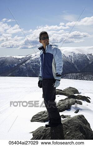 Stock Photo - man standing on snow covered mountain smiling. Fotosearch