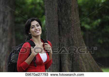 Stock Image - Mid shot of young woman wearing back pack and smiling. Fotosearch